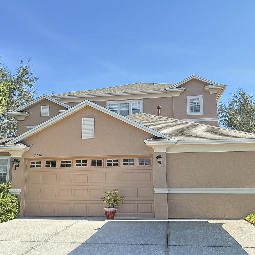 A two-story beige suburban house with a double garage, white trim, and a small potted plant in front of the garage door, under a clear blue sky.