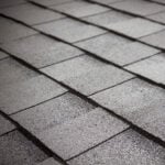 Close-up view of gray asphalt roof shingles arranged in overlapping rows, creating a textured and uniform pattern.