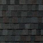 Close-up view of dark gray and black asphalt roof shingles arranged in a neat, overlapping pattern, showing texture and subtle color variations.