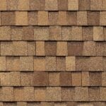 Close-up view of a pattern of brown asphalt roof shingles, arranged in overlapping rows with varying shades of tan and brown.