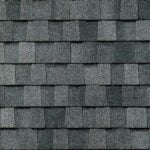 Close-up view of a roof covered with overlapping rectangular dark gray asphalt shingles arranged in neat, horizontal rows. The surface has a rough, textured appearance.