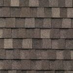 Close-up view of brown asphalt shingles on a roof, arranged in an overlapping pattern with subtle variations in color and texture.