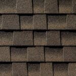 Close-up view of brown asphalt roof shingles arranged in an overlapping pattern, showing their rough, textured surface.