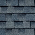 Close-up of blue-gray asphalt shingles arranged in a staggered pattern, showing textured, granulated surfaces and subtle color variations.