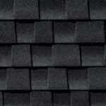Close-up view of dark gray asphalt roof shingles arranged in a staggered pattern, showing coarse, textured surfaces with visible granules.
