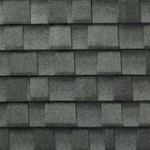 Close-up view of gray asphalt roof shingles arranged in a uniform, overlapping pattern. The surface has a slightly rough texture and a subtle variation in shading.