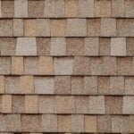 A close-up view of a roof covered with overlapping brown and tan asphalt shingles arranged in a horizontal pattern.