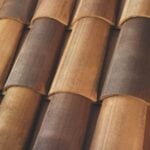 Close-up view of overlapping, curved terracotta roof tiles in various shades of brown and tan, forming a textured and patterned surface.