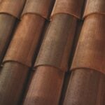 Close-up view of overlapping brown terracotta roof tiles arranged in neat rows, showing their curved shapes and textured surfaces.
