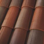 Close-up view of overlapping, brown and reddish clay roof tiles with a textured, lined surface. The tiles are arranged in neat, curved rows.