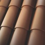 A close-up view of overlapping brown ceramic roof tiles, arranged in a neat, repetitive pattern. The tiles have a curved, semi-cylindrical shape and smooth texture.