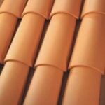 Close-up view of terracotta roof tiles arranged in overlapping rows, forming a repeating pattern with a warm, orange-brown color.