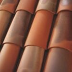 Close-up view of overlapping curved terracotta roof tiles in various shades of brown and orange, arranged in neat, parallel rows.