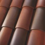 Close-up view of overlapping red and brown curved roof tiles arranged in a repeating pattern, showing smooth surfaces and a glossy finish.