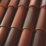 Close-up of overlapping terracotta roof tiles arranged in neat, parallel rows, showing varying shades of reddish-brown and smooth, curved surfaces.