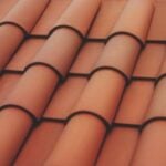 Close-up view of overlapping terracotta roof tiles arranged in neat, horizontal rows, creating a textured pattern. The tiles are a reddish-brown color typical of traditional Mediterranean-style roofing.