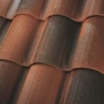 Close-up view of terracotta roof tiles with alternating ridges and grooves, showing a mix of reddish-brown and darker weathered areas.