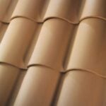 Close-up view of overlapping tan clay roof tiles arranged in neat, parallel rows, creating a wavy, textured surface typical of traditional roof designs.