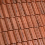Close-up view of a roof covered with overlapping red clay tiles, arranged in neat horizontal rows with visible shadows and slight color variations.