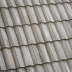 Close-up view of overlapping, wavy beige roof tiles arranged in neat horizontal rows, forming a repetitive textured pattern.