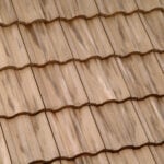 Close-up view of beige ceramic roof tiles arranged in a wavy, overlapping pattern, creating a textured surface. The tiles have slight variations in color and shading.
