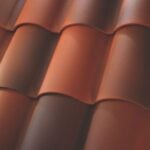 Close-up view of overlapping reddish-brown curved roof tiles, arranged in neat, horizontal rows. The smooth tiles create a textured, patterned surface typical of tiled roofing.