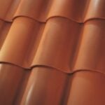Close-up view of overlapping, curved, reddish-orange roof tiles arranged in neat horizontal rows, showing the smooth texture and glossy finish of the tiles.