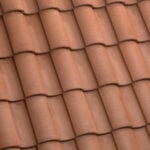 Close-up view of overlapping reddish-brown clay roof tiles arranged in a neat, repeating pattern, forming a traditional tiled roof surface.
