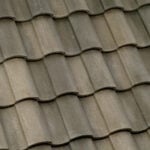 Close-up view of overlapping gray ceramic roof tiles arranged in a wavy, repeating pattern, creating a textured surface on a sloped rooftop.