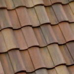 Close-up view of overlapping brown and tan ceramic roof tiles arranged in a repeating pattern, showing the texture and weathered appearance of the material.