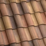 Close-up view of overlapping terracotta roof tiles in shades of brown, orange, and tan, creating a repeating wavy pattern.