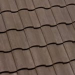 Close-up view of brown, wavy, overlapping roof tiles arranged in horizontal rows, creating a textured and uniform pattern.