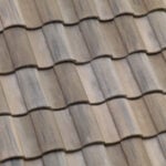 Close-up view of overlapping brown and gray clay roof tiles arranged in neat, horizontal rows, creating a textured and wavy pattern.