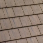 A close-up view of a rooftop with evenly arranged, overlapping rectangular brown tiles, showing their textured surface and neat alignment.