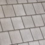 Close-up view of a tiled roof with overlapping rectangular gray tiles arranged in a neat, repeating pattern. The tiles have a smooth texture and are laid in horizontal rows.