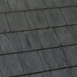 Close-up view of dark gray, rectangular roofing tiles arranged in a staggered, overlapping pattern, creating a uniform and textured surface.
