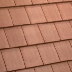Close-up of a roof with overlapping rectangular terracotta tiles arranged in neat, horizontal rows. The tiles have a slightly textured surface and uniform color.
