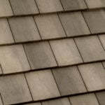 Close-up view of overlapping concrete roof shingles arranged in neat horizontal rows, displaying a uniform pattern with muted gray and beige tones.