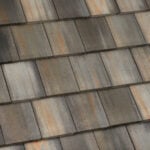 Close-up view of weathered, multicolored roof shingles with shades of gray, brown, and rust, arranged in a neat, overlapping pattern.