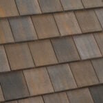 Close-up view of a roof with overlapping rectangular brown and gray shingles, showing a weathered and textured surface.