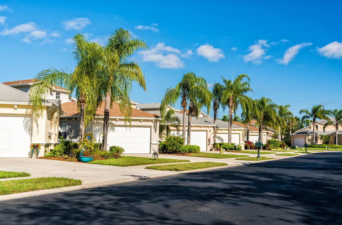 A row of modern suburban houses with attached garages lines a clean, wide street beneath a clear blue sky—reminding many homeowners to consider how often you should replace your roof in Florida’s sunny, palm-tree-lined neighborhoods.