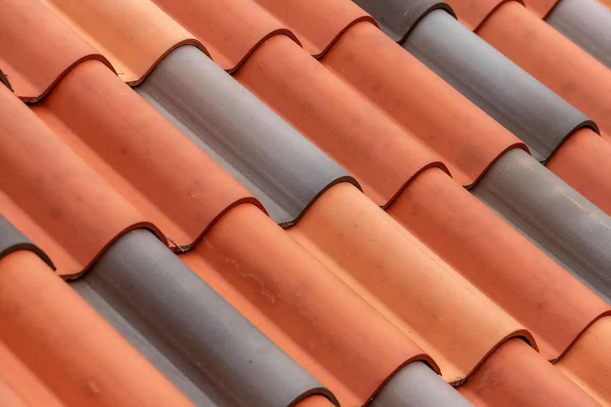 Close-up view of a barrel tile roof featuring alternating rows of reddish-brown and gray curved tiles, arranged in a repeating wave-like pattern.