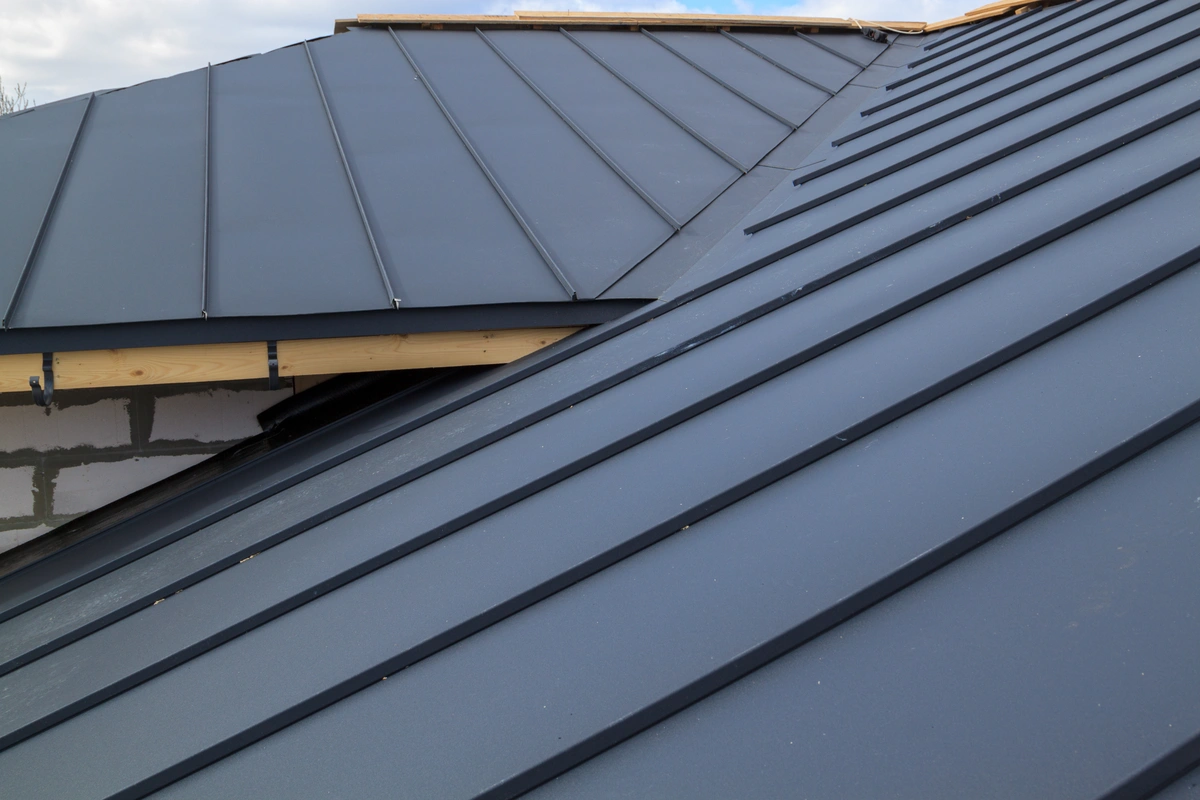 Close-up view of a modern stone coated steel roofing system with clean, straight lines and a matte gray finish on a residential building, partially showing the edge and wooden roof framing.