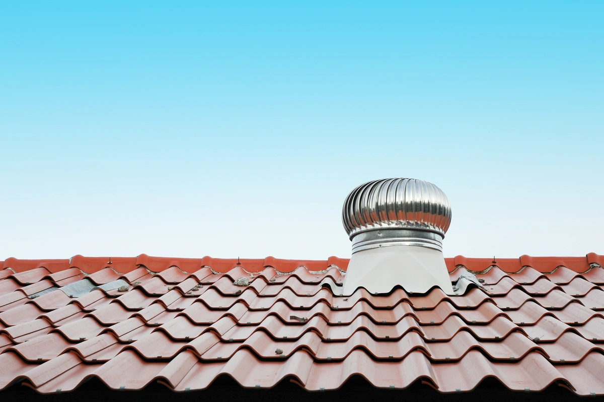 A red tiled roof with a silver metal roof vent showcases excellent roof ventilation under a clear blue sky.