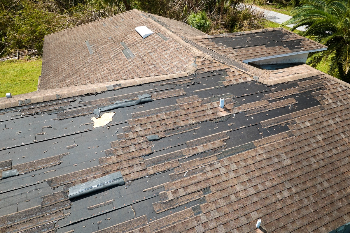 An asphalt shingle roof with large sections of shingles missing