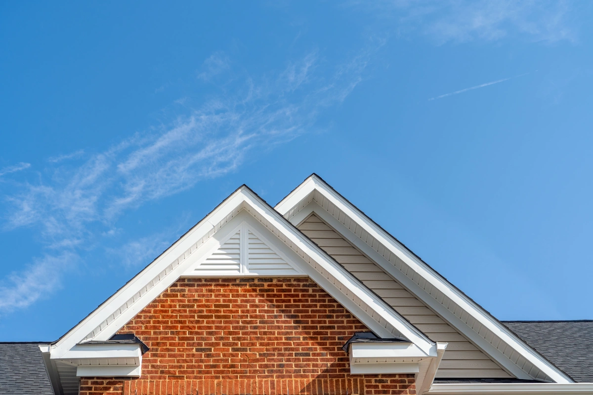 Close-up of the pointed roofs of a brick house with white trim and expertly finished fascia repair, set against a clear blue sky with wispy clouds.