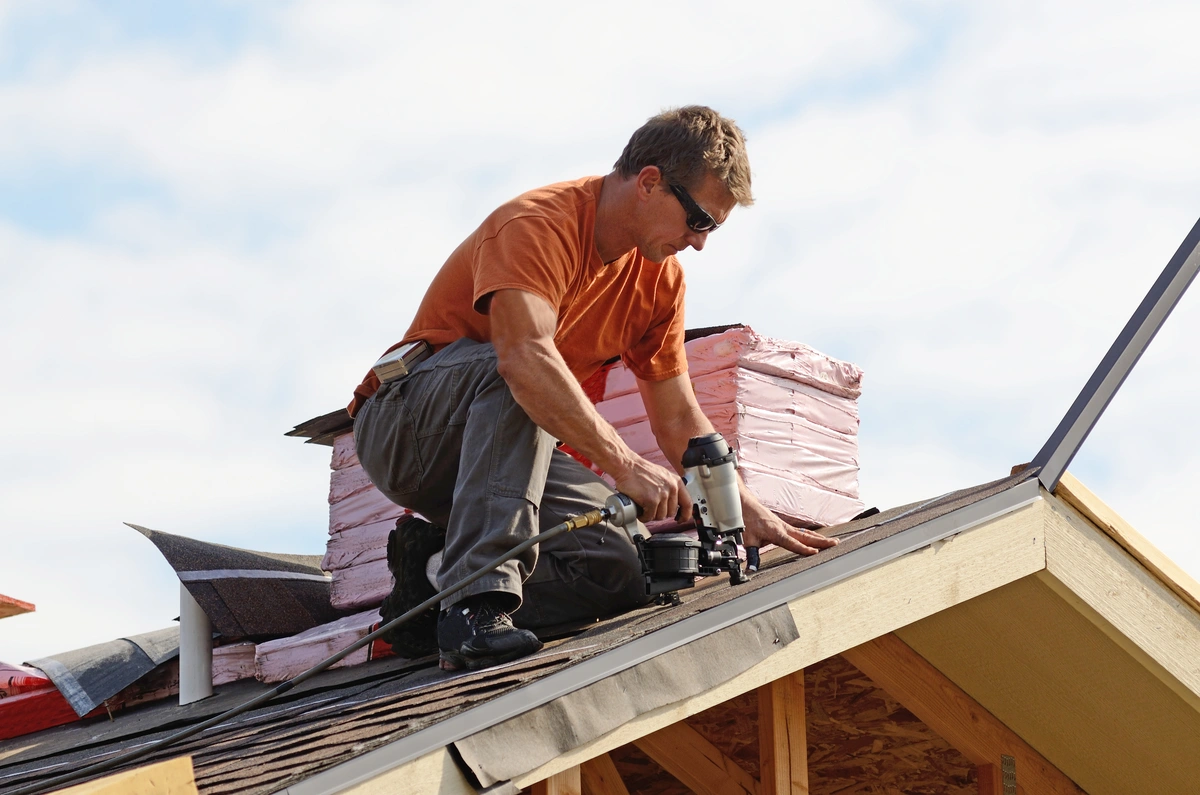 worker installing roof shingles with a nail gun