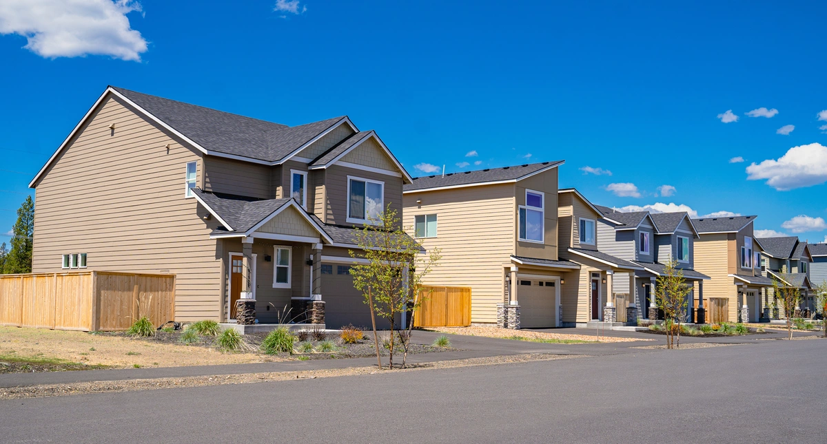 A row of modern suburban houses with beige siding and dark roofs lines a quiet street under a bright blue sky with scattered clouds, showing well-kept landscaping—key for preventing roof rats in Florida neighborhoods.
