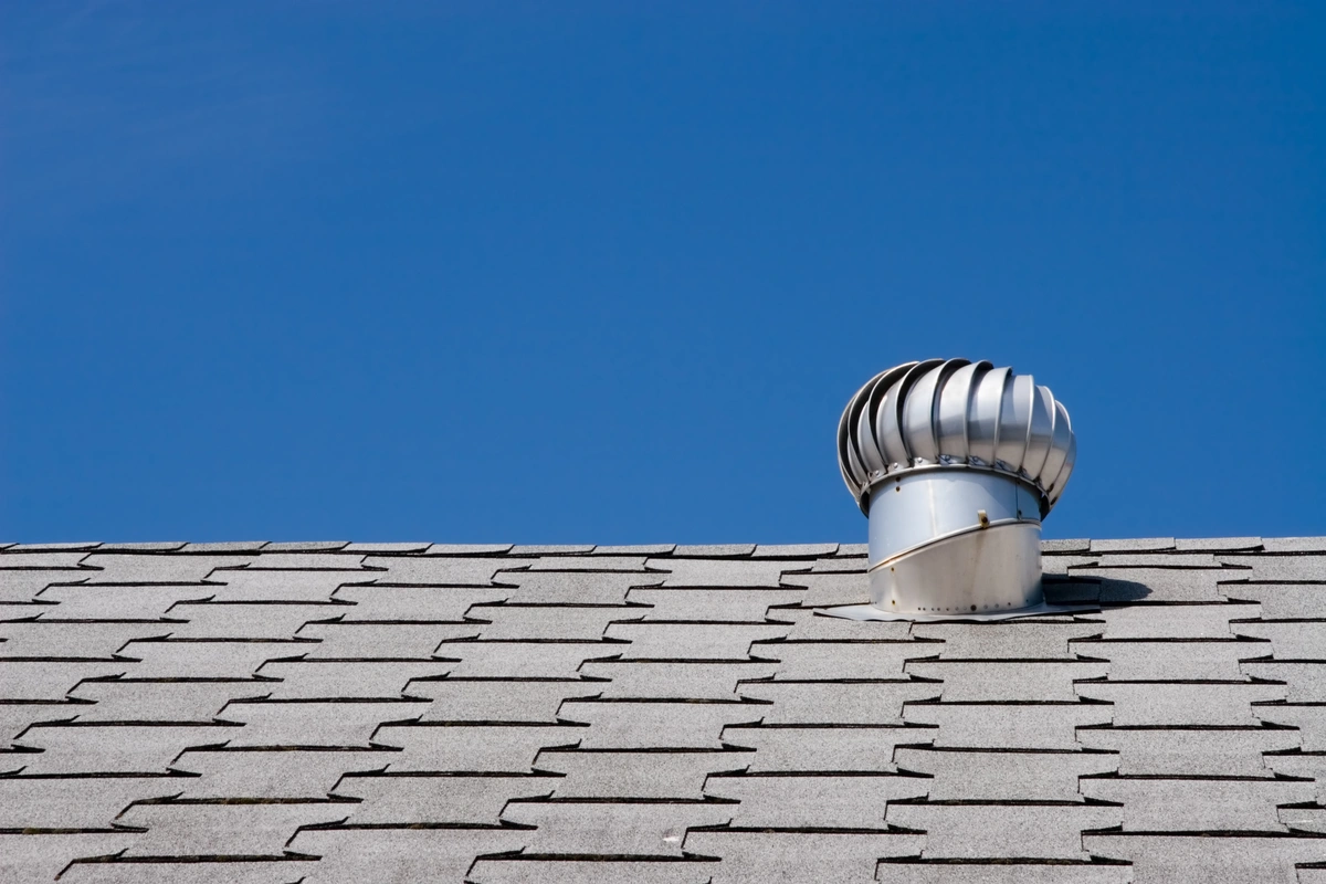 A silver turbine, one of the popular types of roof vents, is installed on a gray shingle roof under a clear blue sky.