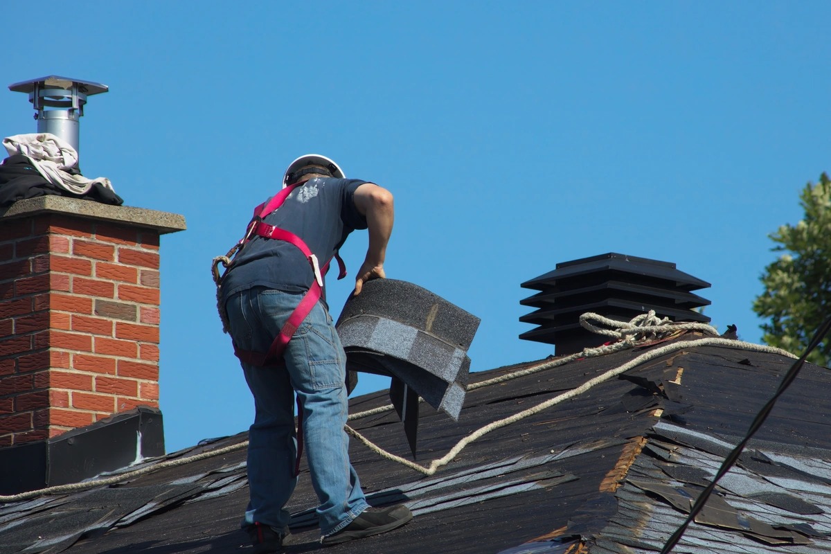 Construction worker removing asphalt shingles and repairing roof